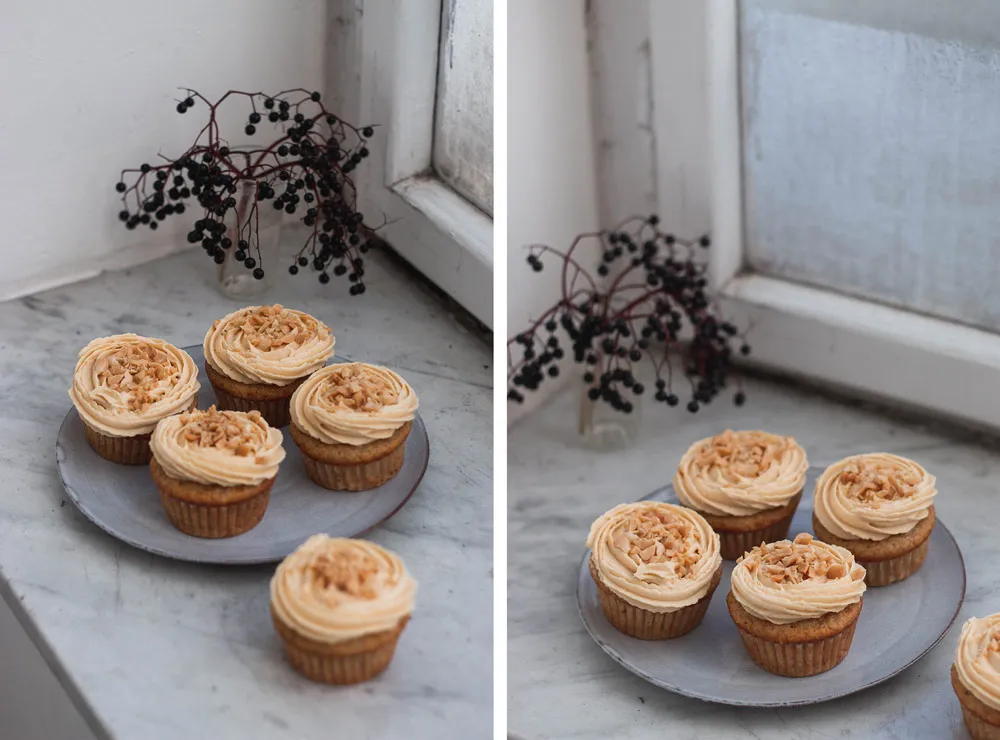 Banánové cupcakes s arašídovým krémem a drcenými arašídy na šedém talíři na mramorovém parapetu u okna s větvičkou bobulí.