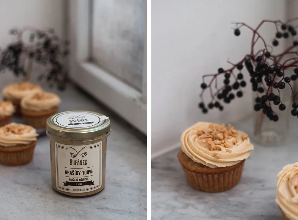 Sklenice arašídového másla Šufan v popředí a cupcake s věncovitým arašídovým krémem posypaný drcenými arašídy na mramoru.