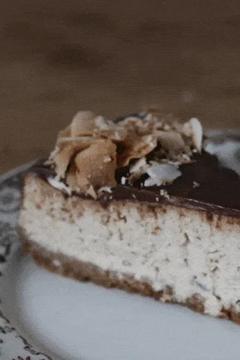 Řez banánového cheesecaku s čokoládovou polevou a kokosem na talíři s modrým květinovým vzorem