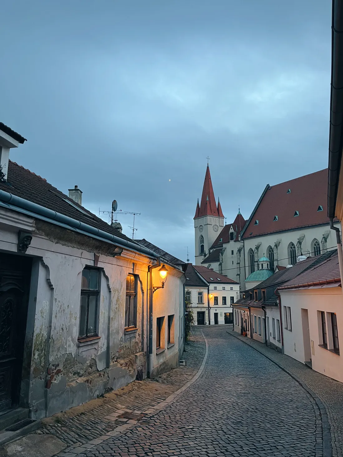 Úzká dlážděná ulička v Znojmě za soumraku s kostelem sv. Mikuláše a vysokou červenou věží
