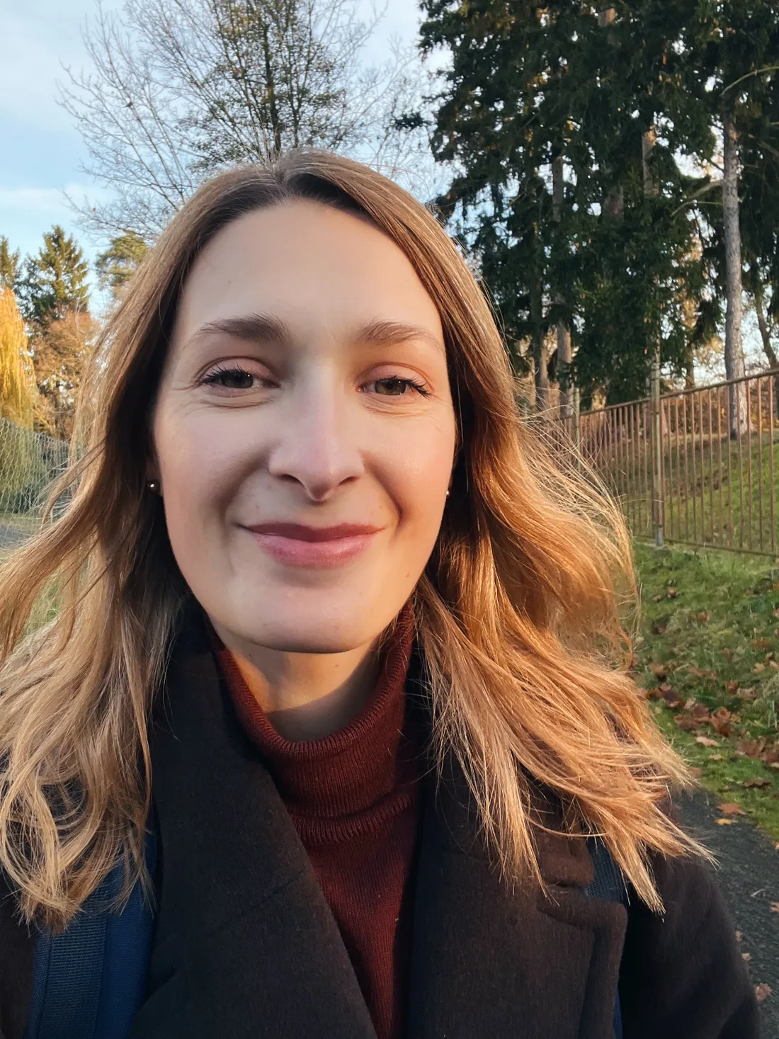 Selfie usmívající se blond ženy v kabátu v parku s podzimním listím a stromy