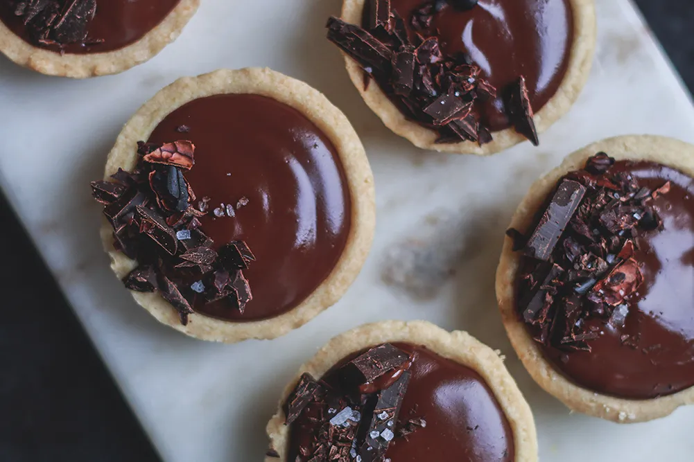 Pět čokoládových tartaletek s ganache, čokoládou a vločkovou solí na mramoru, detailní záběr