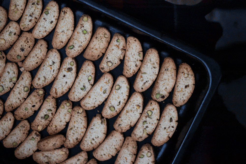 Čerstvě upečené biscotti s pistáciemi a pomerančovou kůrou na černém plechu – detailní záběr na řady křupavých plátků.