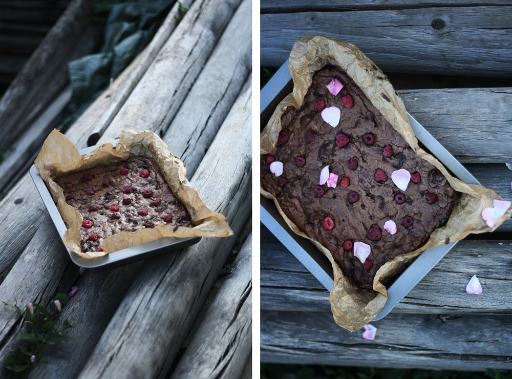 Čokoládové brownies s malinami a růžovými okvětními lístky v pekáčku na starých dřevěných kládách venku.