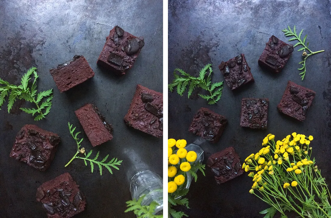Brownies z červené řepy s čokoládou na tmavém podkladu, doplněné zelenými bylinkami a žlutými květy vratiče.