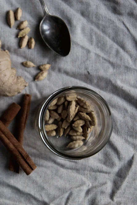 Hrnek chai masala a koření – zázvor, skořice, kardamom a hřebíček – na lněném ubrusu shora