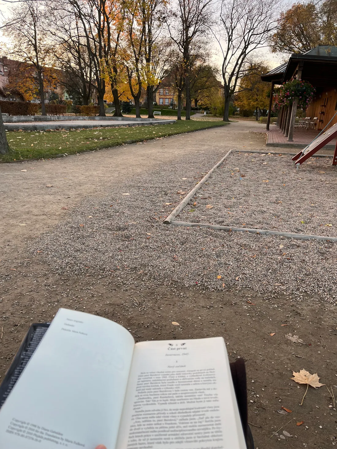 Otevřená kniha v ruce na procházce v parku s podzimními stromy a pískovou cestičkou