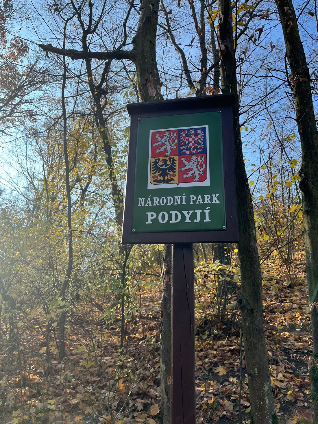 Dřevěná tabule Národní park Podyjí se státním znakem v podzimním lese s opadaným listím