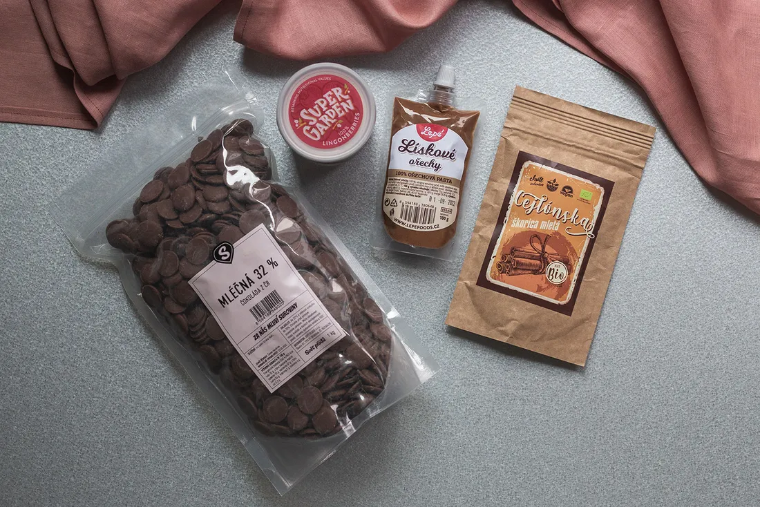 Ingredience na pečení: mléčná čokoláda, brusinky Super Garden, lísková pasta a skořice na šedém podkladu