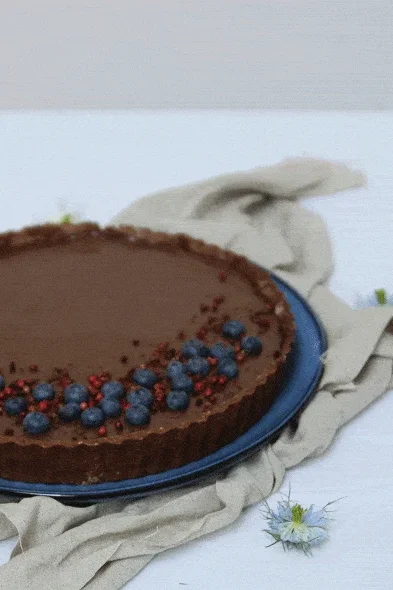 Čokoládový koláč s borůvkami a červeným rybízem na modrém talíři s květy černuchy.