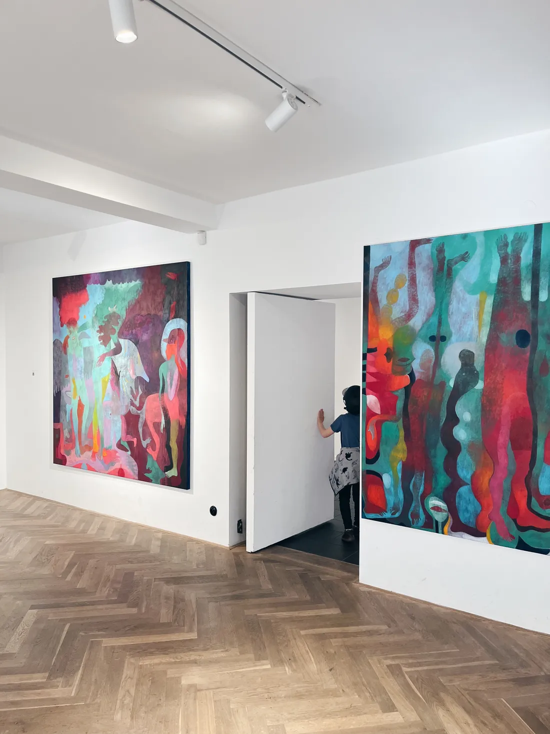 Galerie s velkými surrealistickými obrazy a dítětem mizejícím bílými dveřmi mezi nimi