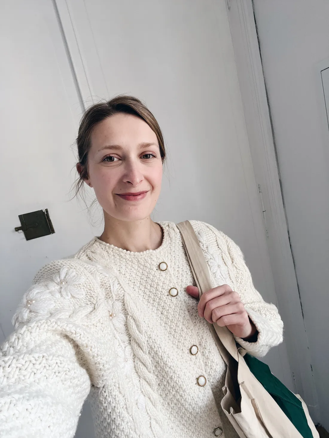 Selfie usmívající se ženy v krémovém pleteném kardiganu s květinovými vzory a plátěnou taškou