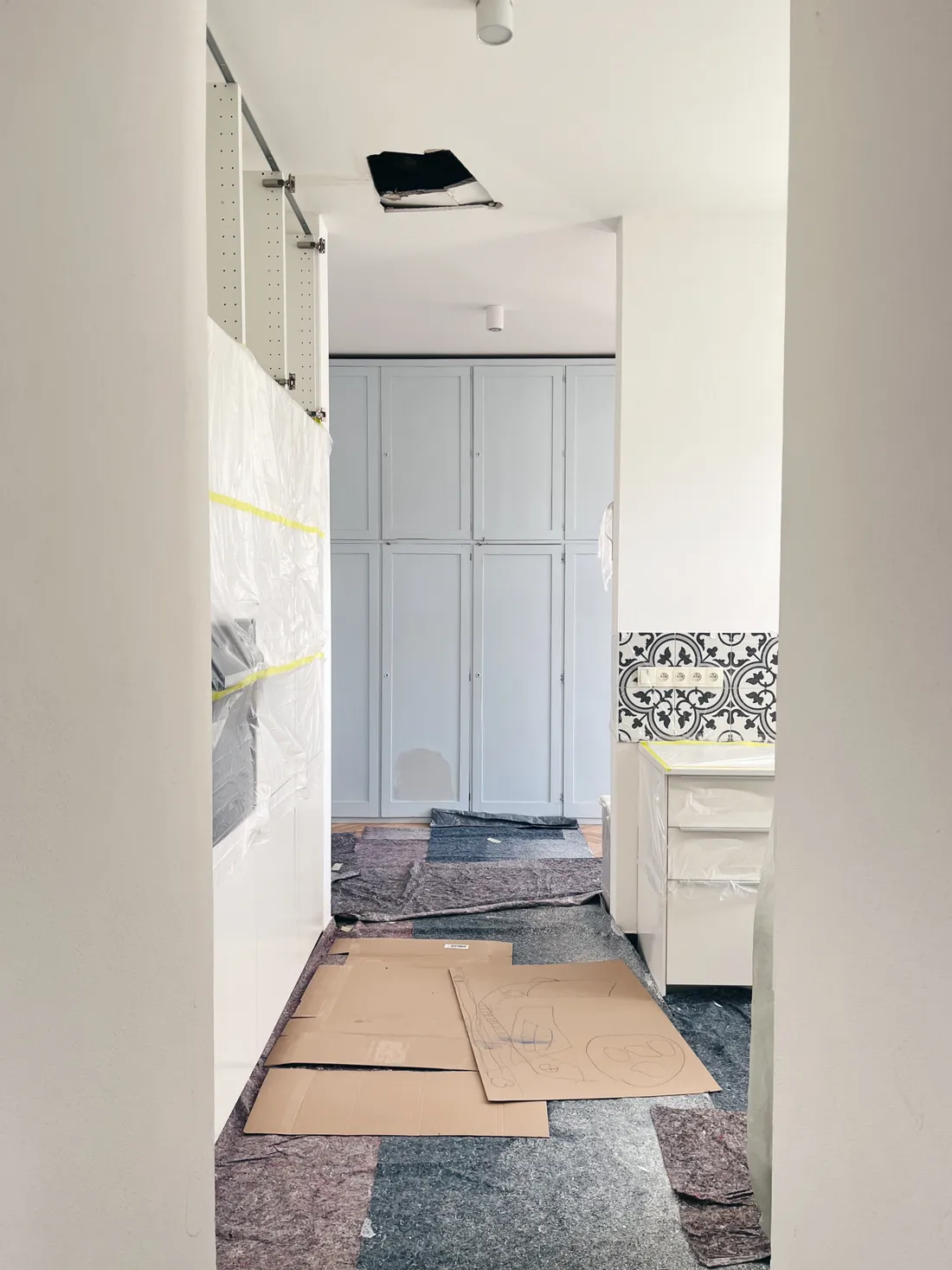 Kuchyně v rekonstrukci s novými bílými skříňkami zabalenými folií a kartony na podlaze