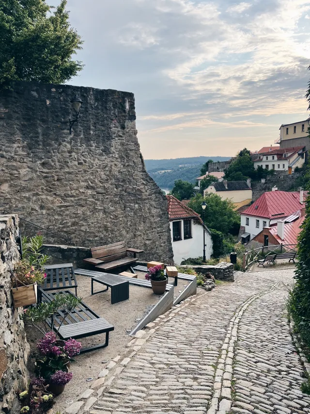 Pohled shora na lněné kalhoty s modrým vzorem, koženou kabelkou a černou botou