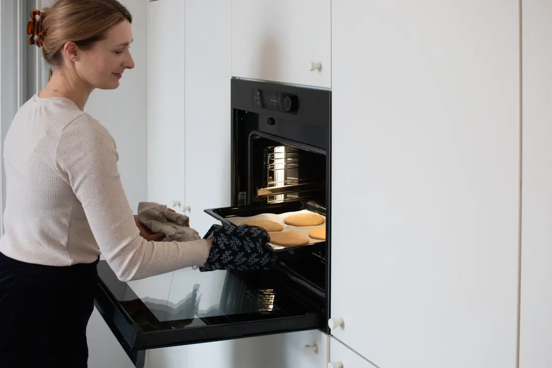 Usmívající se žena vytahuje z trouby plech se čtyřmi zlatými upečenými plackami