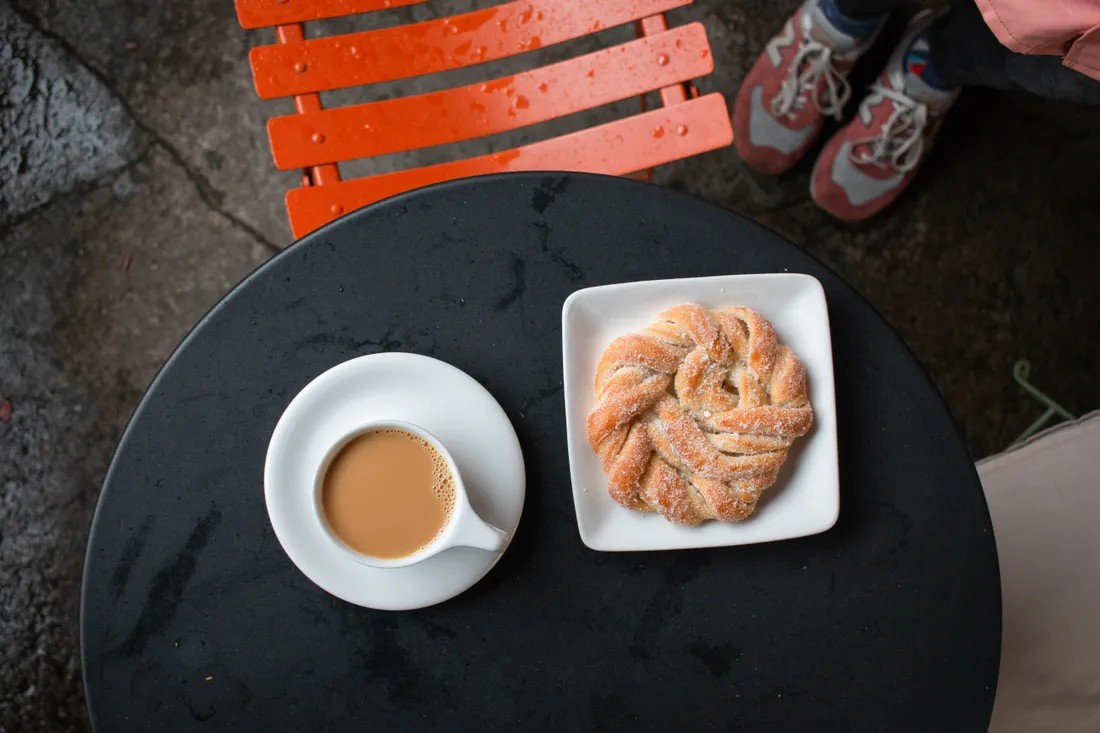 Šnek a šálek kávy na černém kavárenském stolku venku – fika za deštivého počasí.