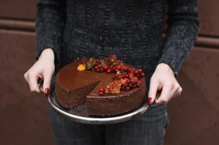 Čokoládový cheesecake s chybějícím kouskem zdobený červenými bobulemi a podzimními lístky na stříbrném podnosu