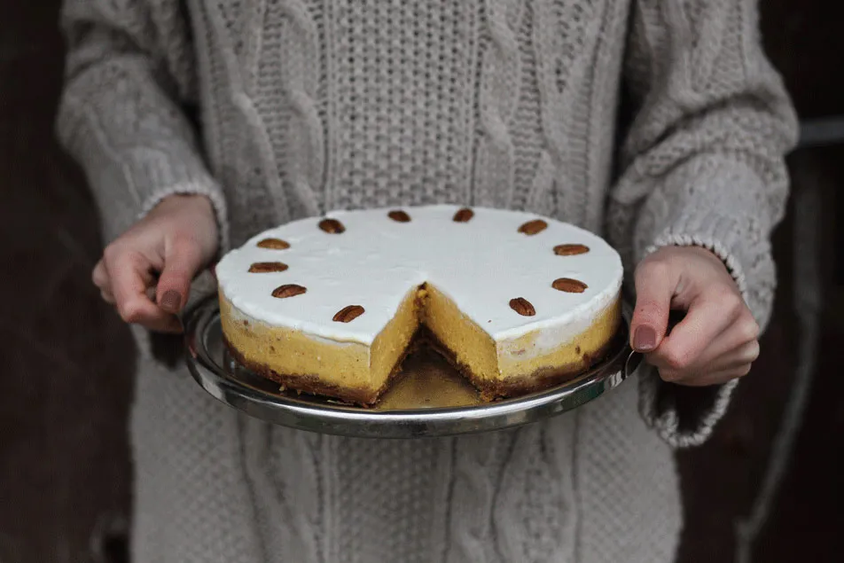 Dýňový cheesecake s bílým krémem a pekanovými ořechy na stříbrném podnosu držený v rukou v pleteném svetru
