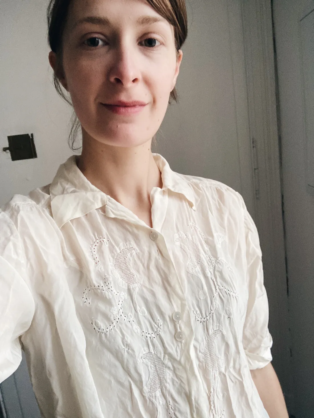 Selfie ženy v krémové vintage halince s bílým krajkovým vyšíváním a openwork detailem na hrudi proti světlé stěně