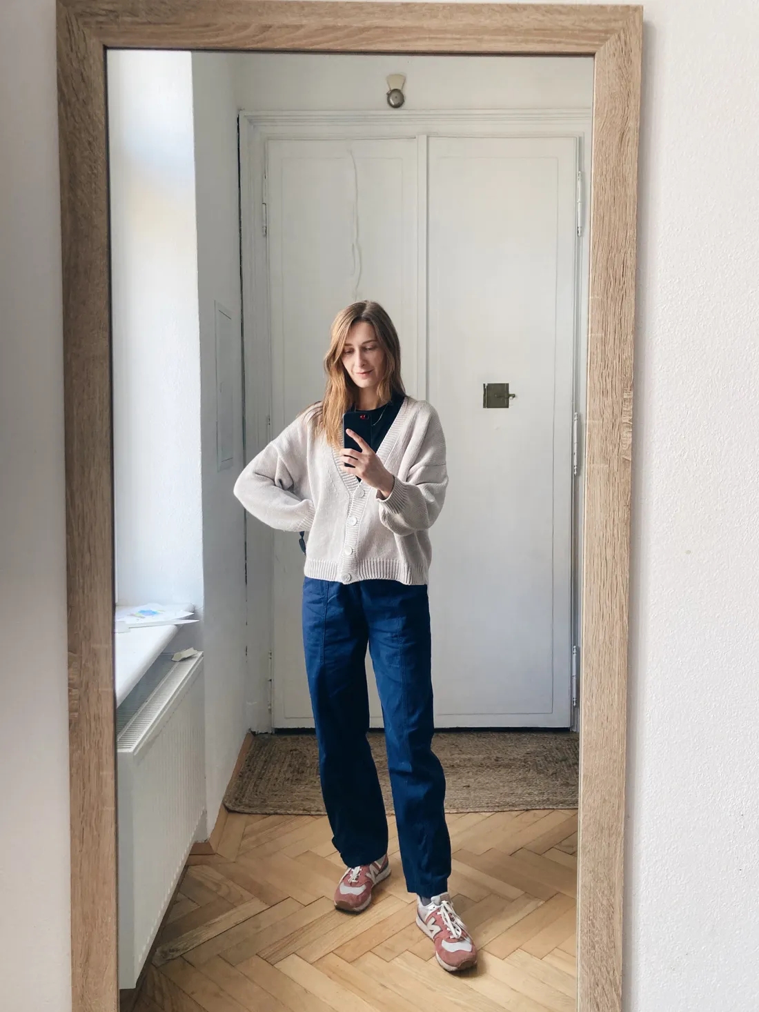 Zrcadlové selfie s béžovým kardigánem, tmavým tričkem, širokými tmavě modrými kalhotami a růžovobílými teniskami New Balance