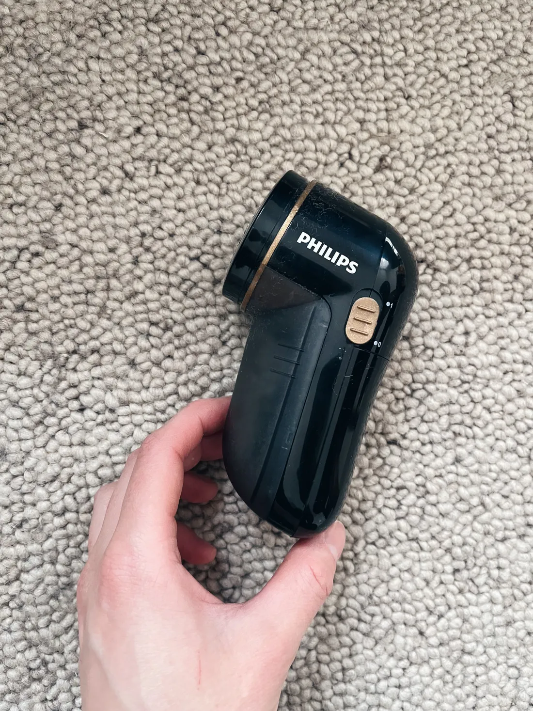 Ruka drží černý odžmolkovač Philips nad světle šedým kobercem s uzlíkovou strukturou