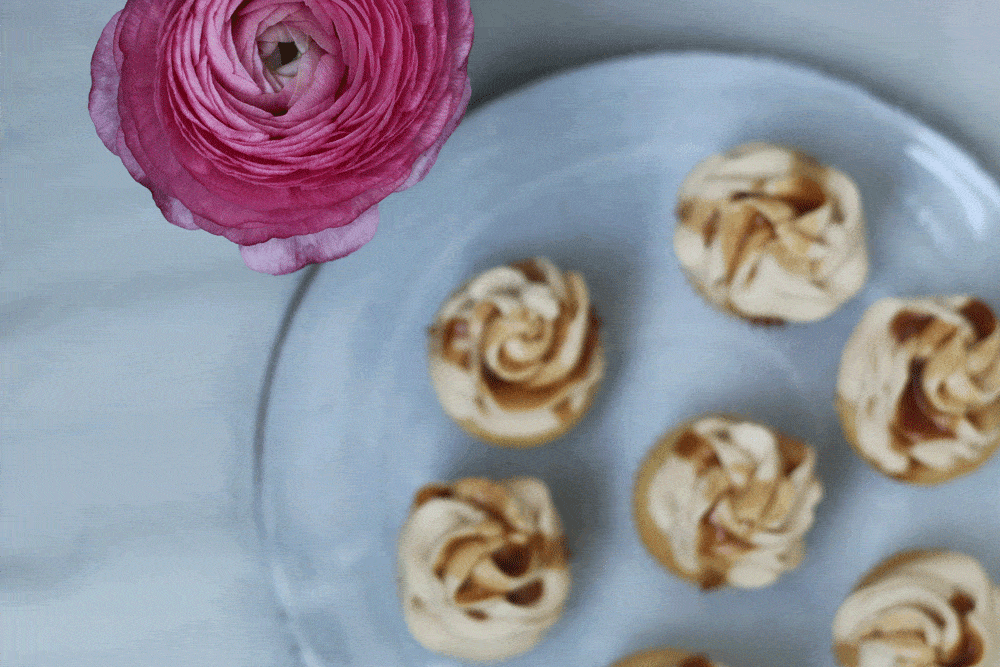 Karamelové cupcakes s dvoubarevným krémem na světle modrém talíři, v rohu růžový pryskyřník