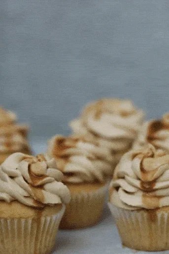 Sedm karamelových cupcakes s hnědou polevou na světle modrém talíři.