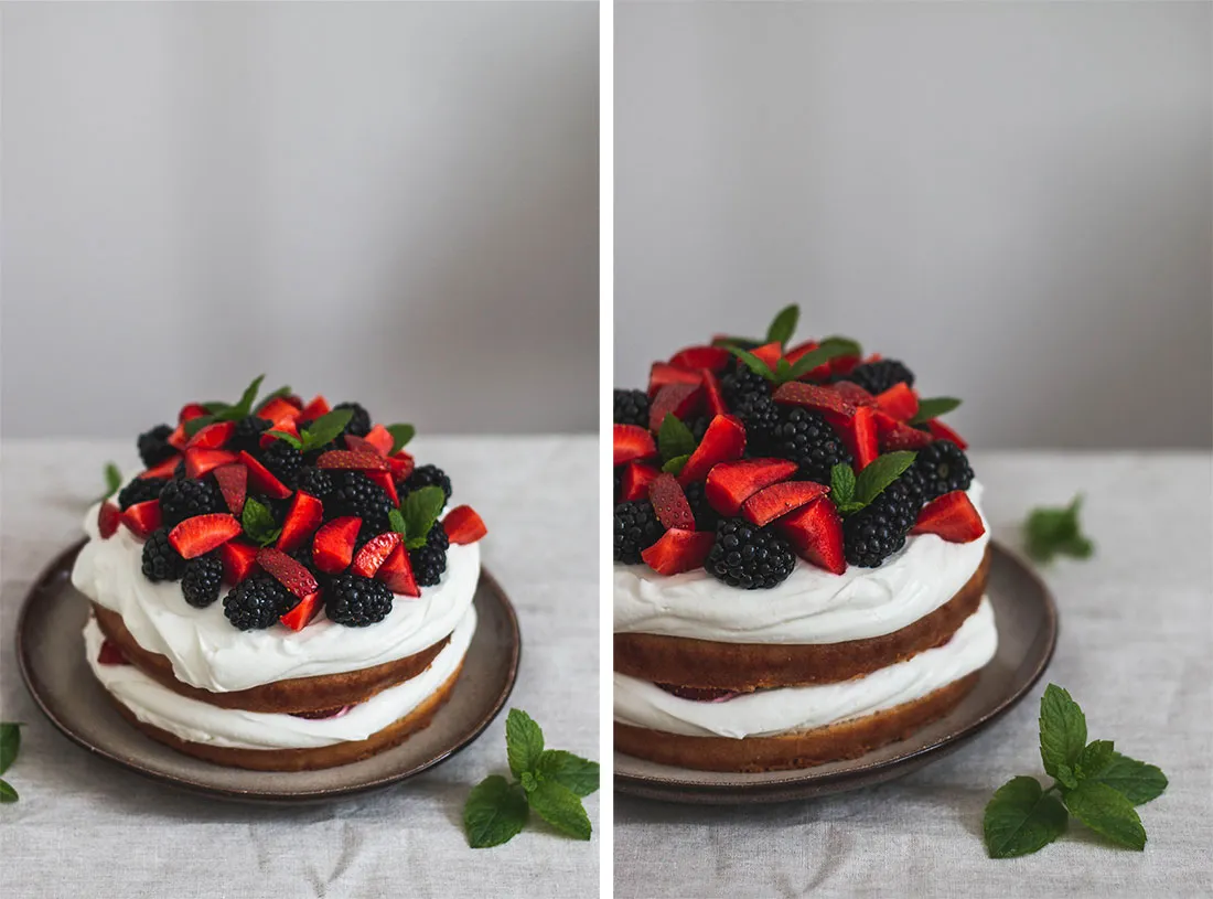 Dvoupatrový naked cake se šlehačkou, ostružinami, jahodami a mátou na tmavém talíři na lněném ubrusu.