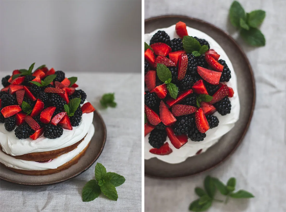 Borůvkový naked cake shora a z boku – bílý krém, ostružiny, jahody a máta na tmavém talíři.