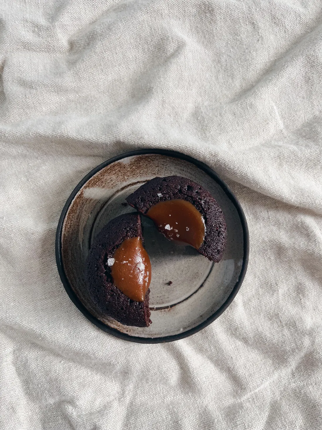 Rozpolcený čokoládový muffin s tekoucí slaným karamelem a vločkami mořské soli na talíři.