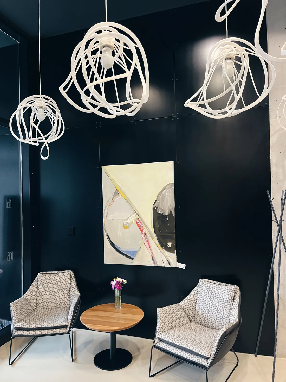 Moderní kavárna se dvěma vzorovanými křesly, abstraktním obrazem a bílými designovými lustry