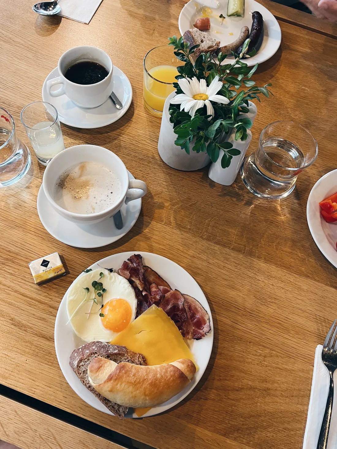 Snídaňový stůl s volským okem, slaninou, sýrem, croissantem, kávou a kapucínem