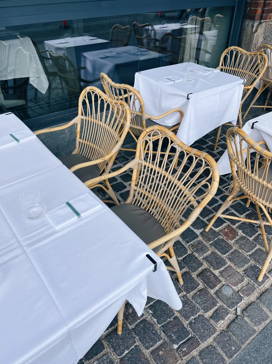 Proutěné židle a stoly s bílými ubrusy na dlážděné terase kodaňské restaurace.