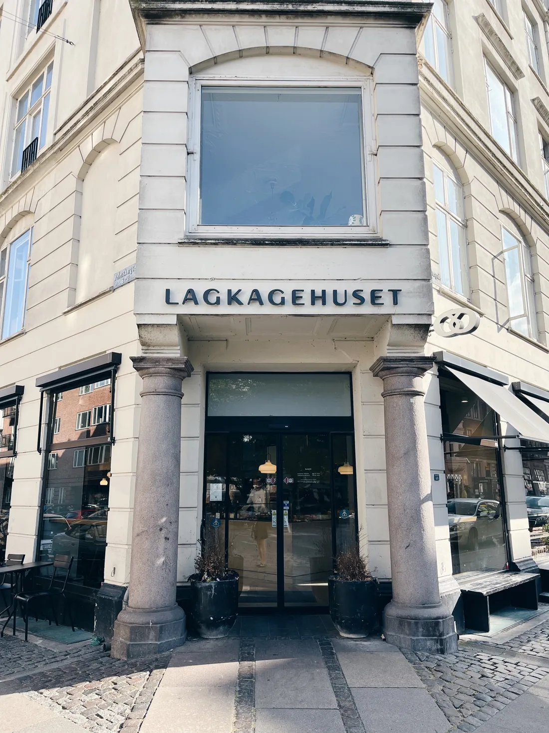 Vstup pekárny Lagkagehuset mezi kamennými sloupy na rohu Vesterbrogade, v chodníku dlažba.