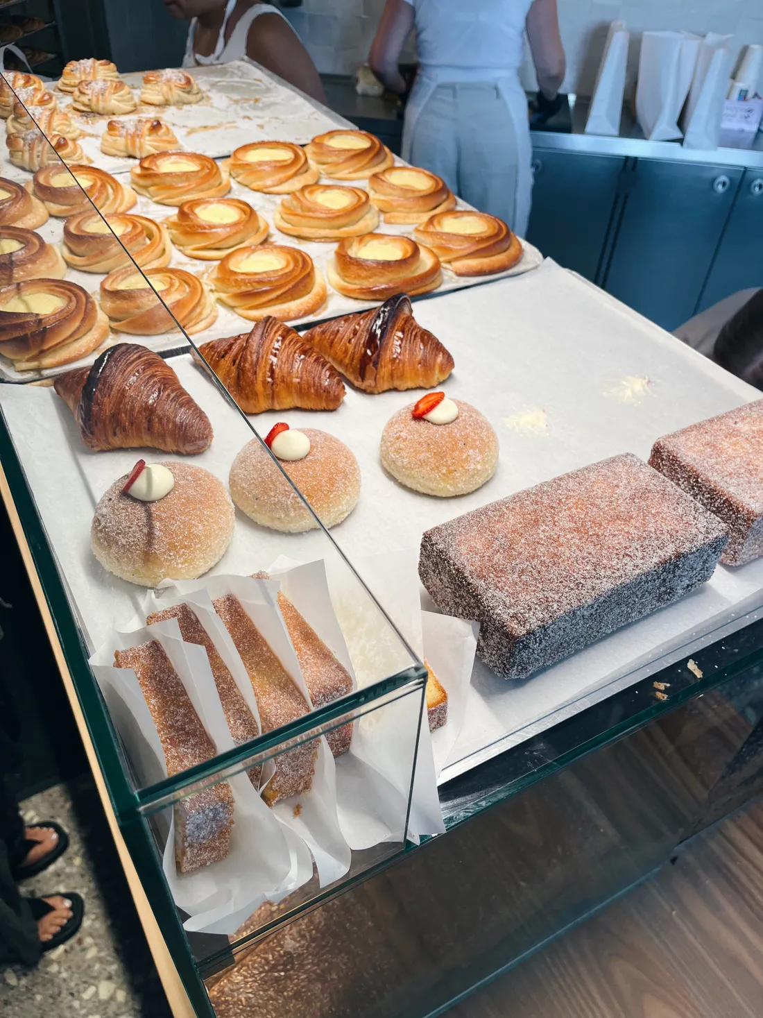 Vitrína s croissanty, šneky s krémem, cukrovými bulky a cukrovými dorty na papíru v pekárně.