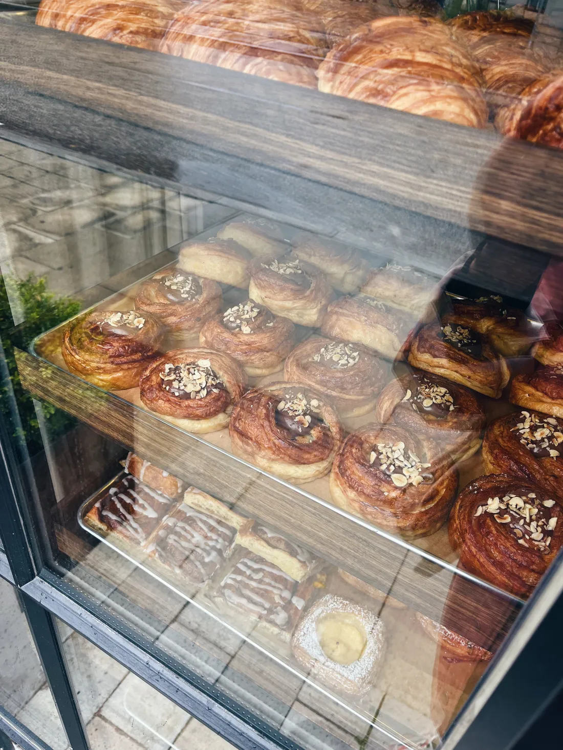 Vitrína pekárny se spirálovými koláčky s čokoládou a ořechy, croissanty a čtvercovým koláčem s krémem.
