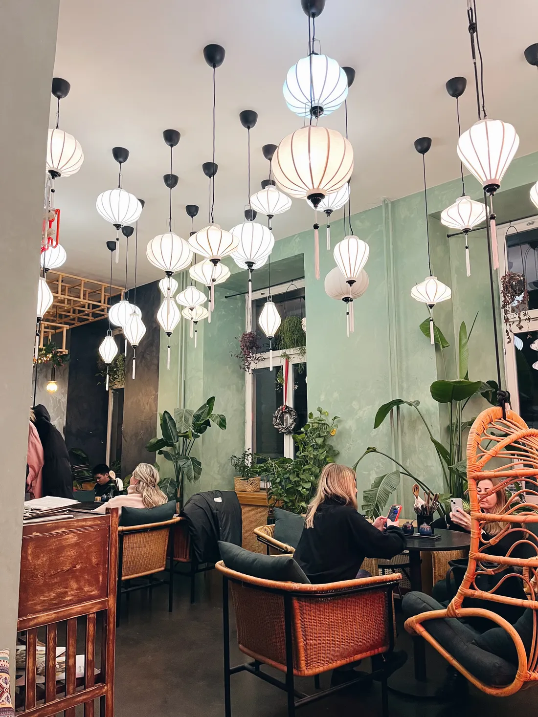 Restaurace s desítkami bílých lampionů, zelenými stěnami a proutěnými křesly.