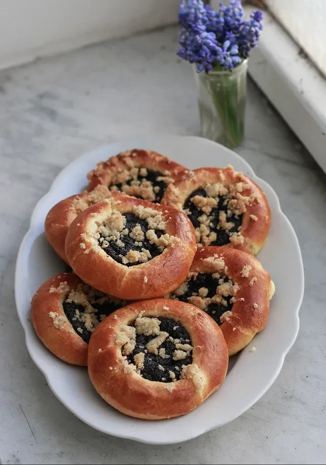 Kynuté koláče s mákem a drobenkou na bílém talíři, v pozadí modré květy.