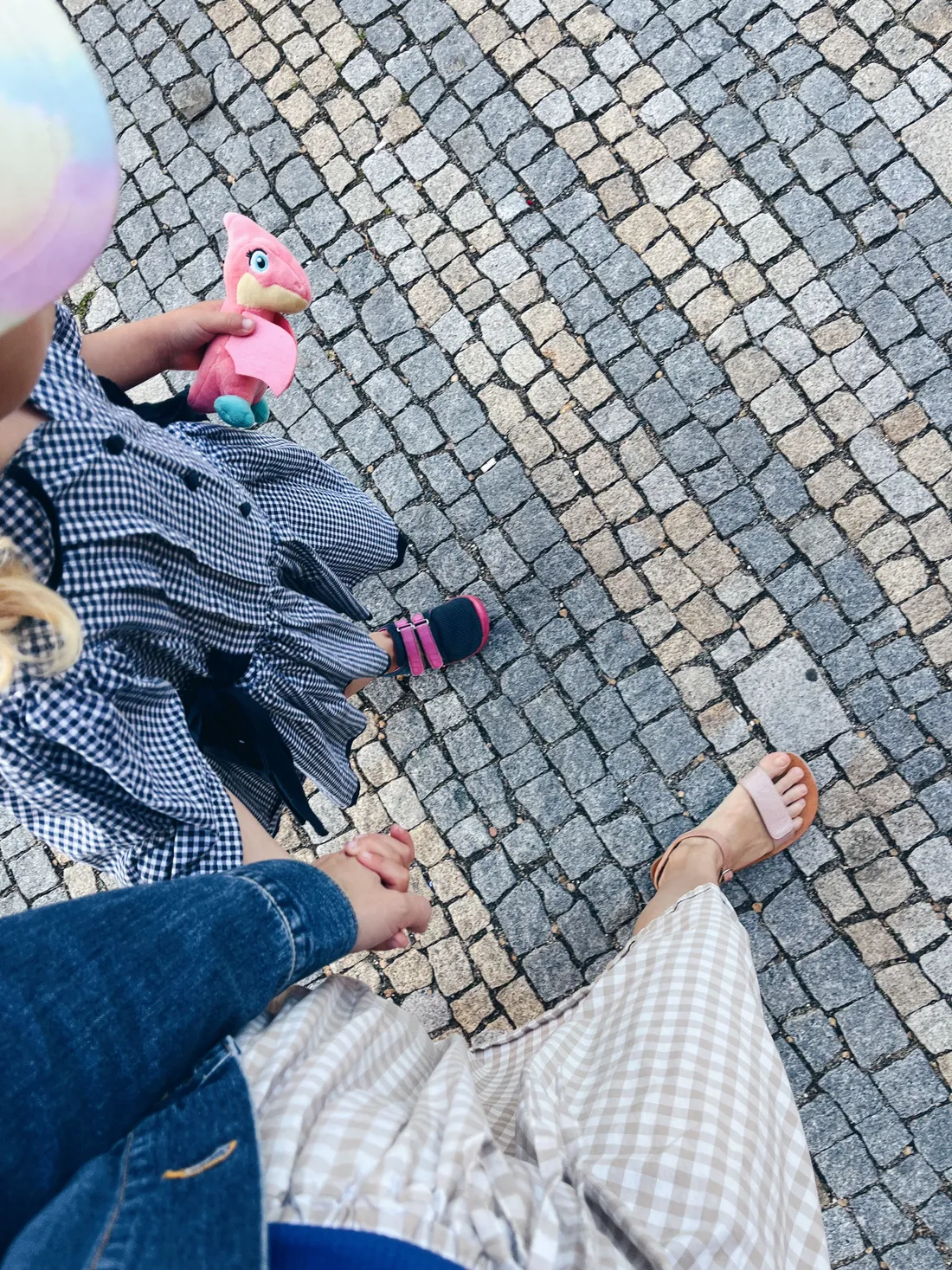 Ruka v ruce s dítětem na dláždění, kostým v kostkách a růžová plyšová dinosauřička.