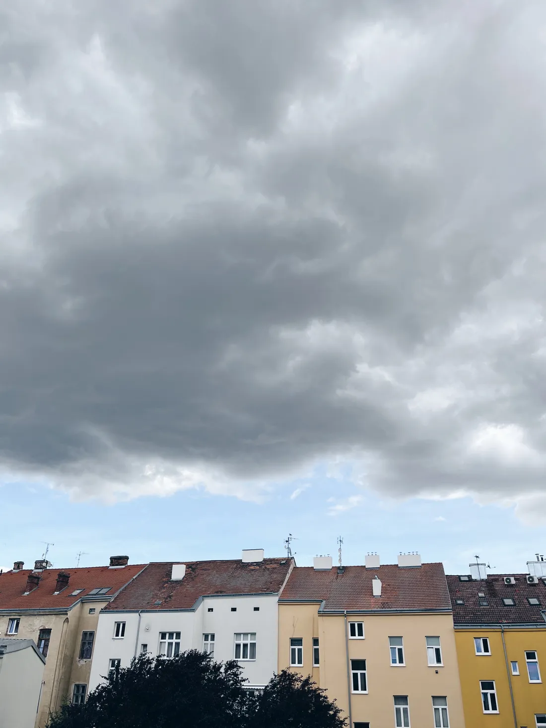 Řada barevných městských domů s červenými střechami pod tmavou oblačnou oblohou.
