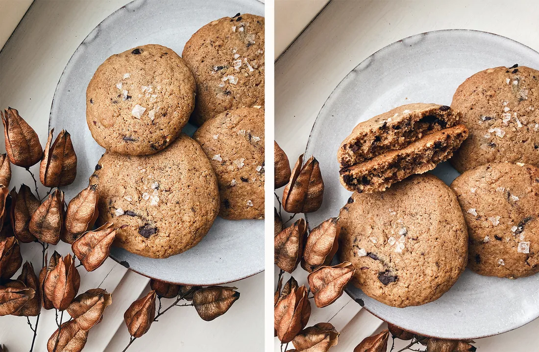 Lískooříškové cookies s čokoládou a solí na šedém talíři, jedna rozlomená ukazuje vláčné těsto uvnitř.