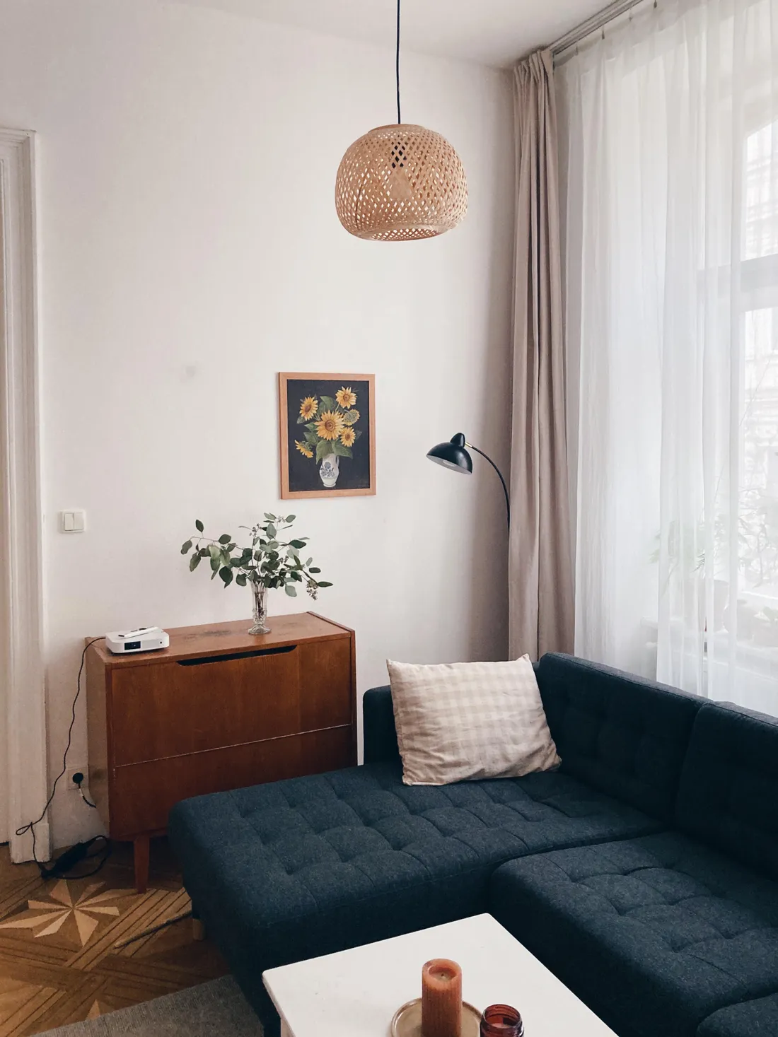 Obývací kout s obrazem slunečnic nad skříní, sedačkou a závěsy u okna s jarním světlem