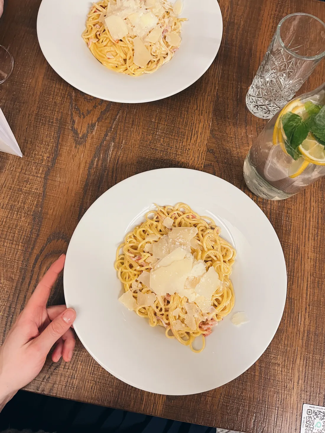 Dva talíře špaget carbonara s parmazánem, sklenice vody s citronem a mátou.