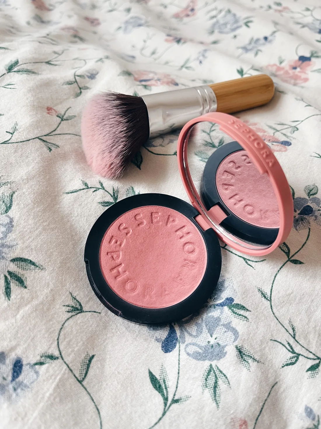 Otevřená růžová rtěnka Sephora a štětec na květované látce, pohled shora.