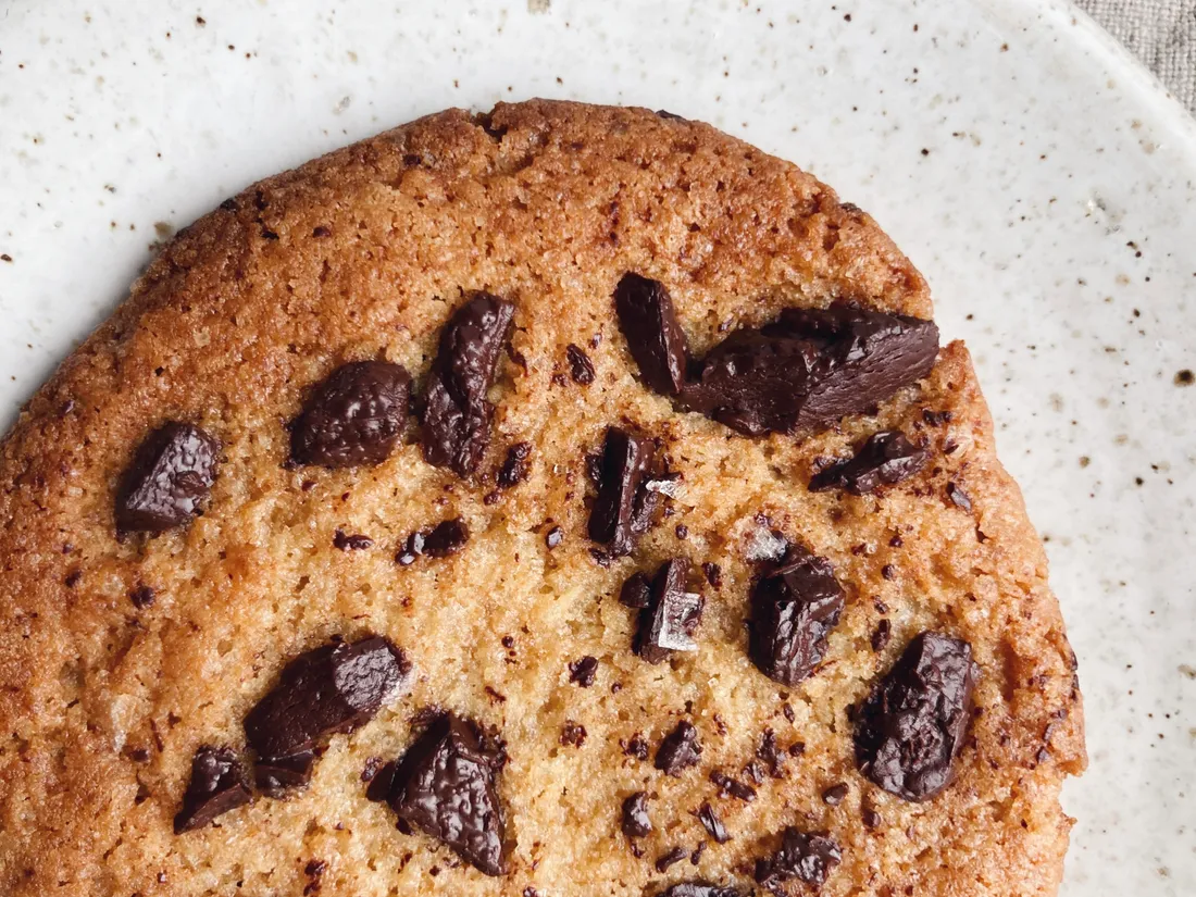 Detail jedné miso cookie s velkými kousky čokolády a solí na světlém talířku s jemnými tečkami.