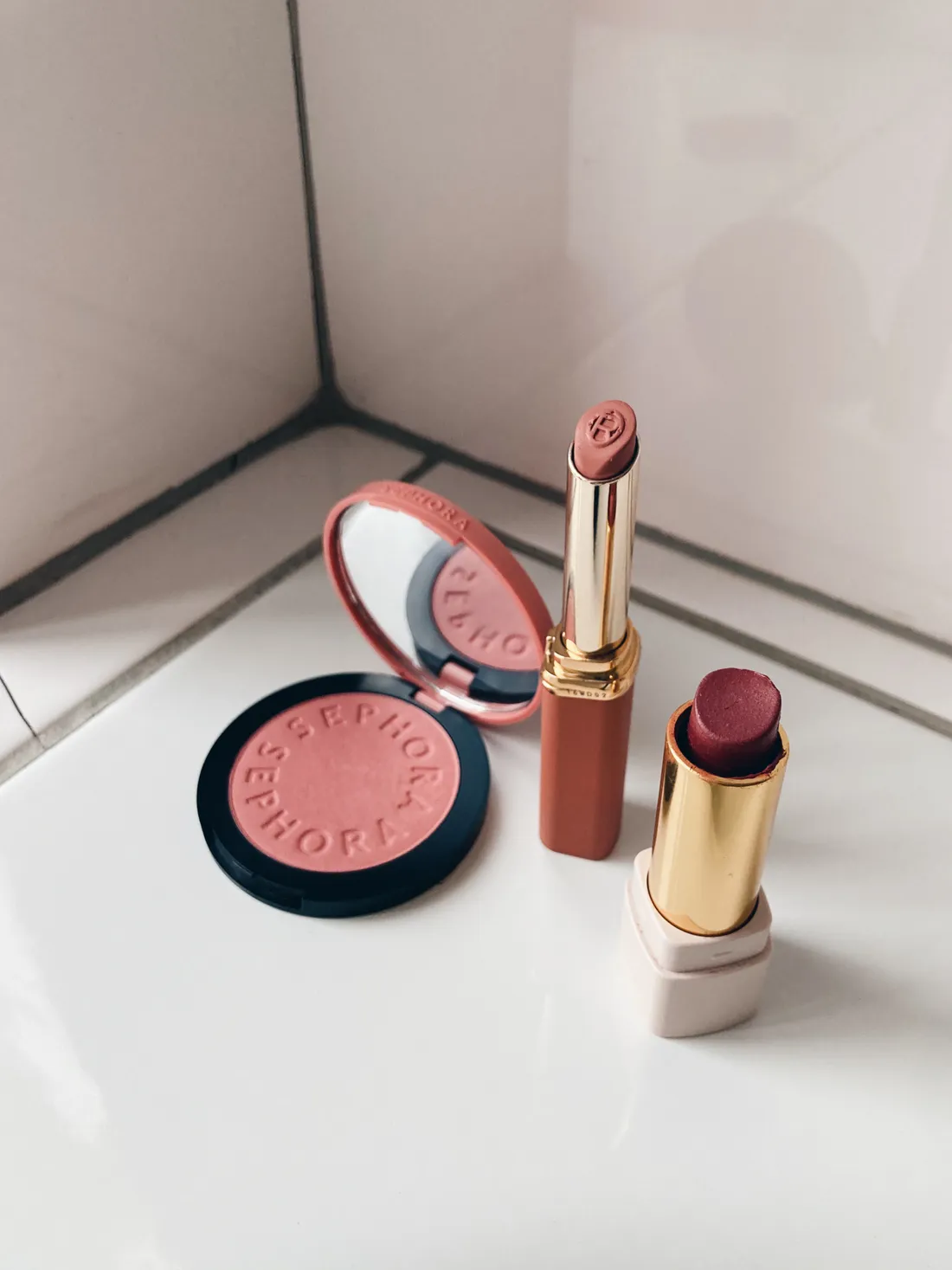 Otevřená tvářenka Sephora a dvě rtěnky v odstínech růžové a vínové na bílých dlaždicích.