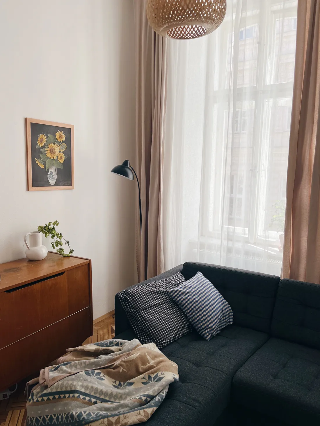 Obývací pokoj s tmavě šedou pohovkou, dřevěnou komodou a obrazem slunečnic u okna.