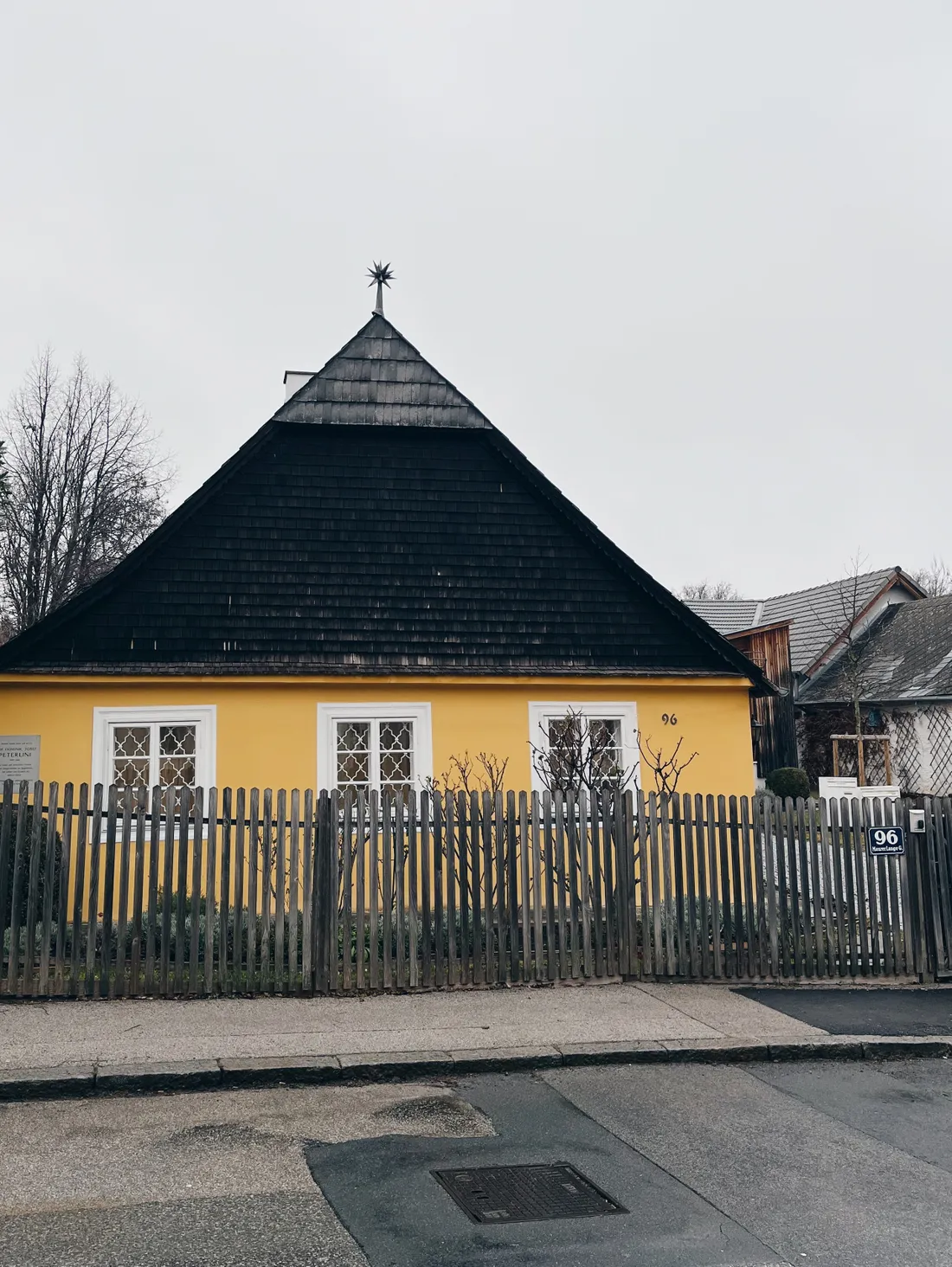 Žlutý domek číslo 96 s vysokou tmavou střechou a hvězdou na vrcholu za dřevěným plotem.