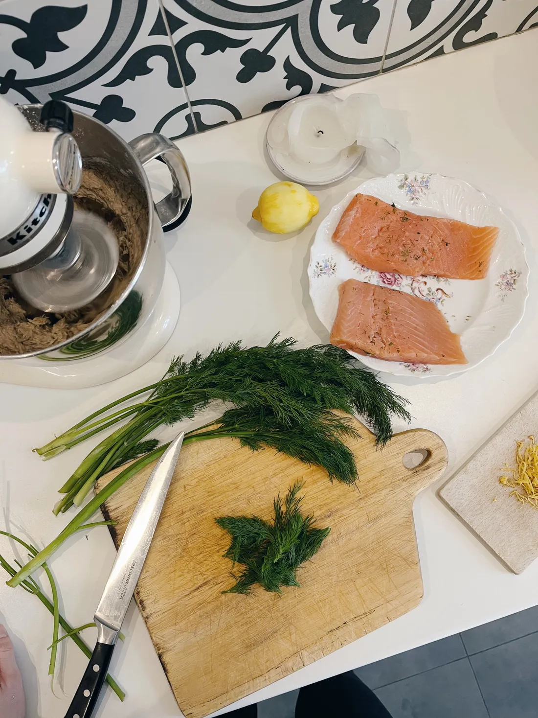 Syrové filety lososa, čerstvý kopr, citron a robot KitchenAid s těstem na bílé lince.