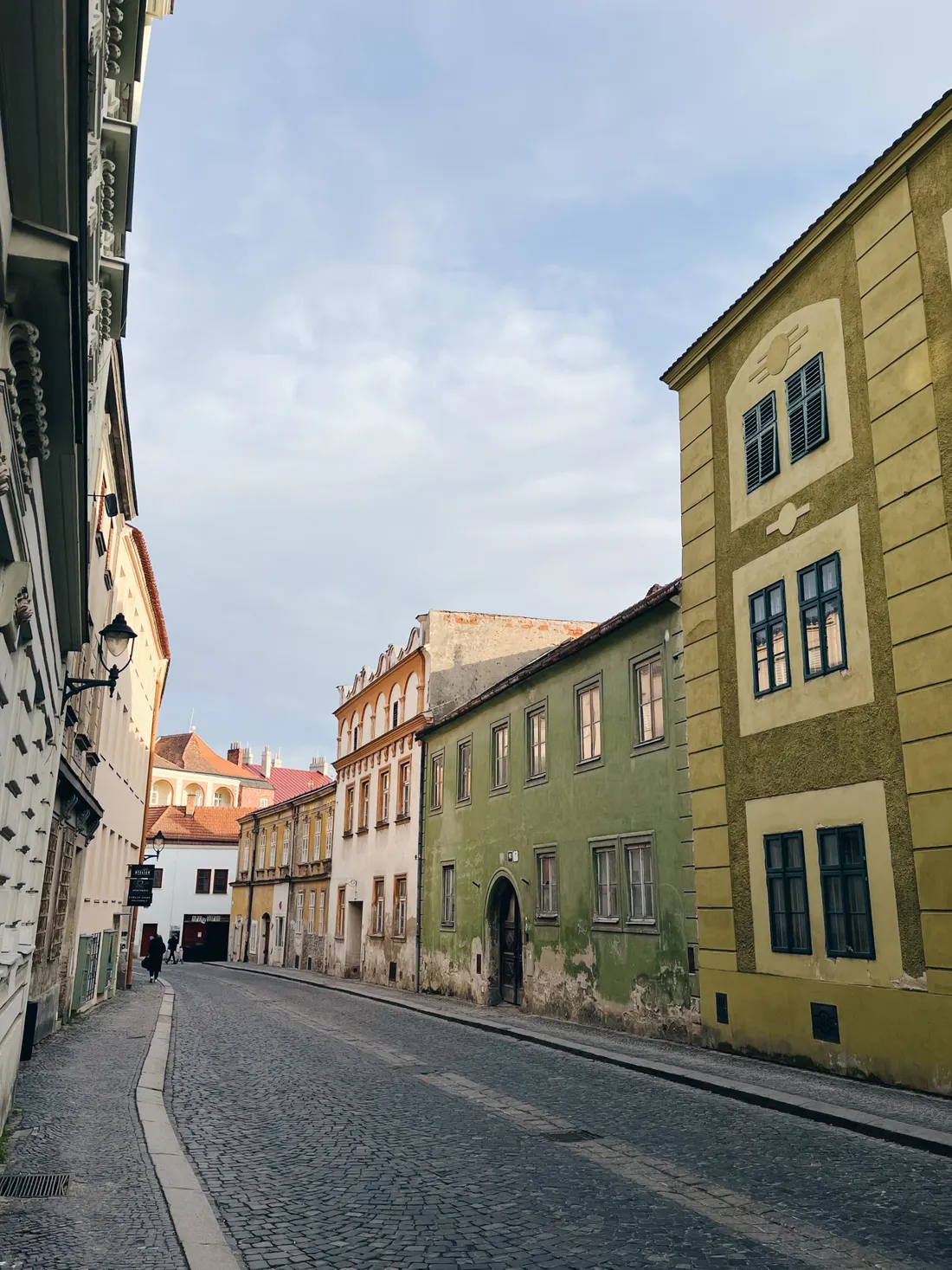 Úzká dlážděná ulička mezi historickými domy v žluté a zelené barvě.